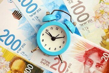 Israel New Shekels banknotes and alarm clock. The current Israel money bills and clock lies on table