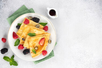 Thin pancakes with berries, mint leaves and maple syrup on a gray background. Top view. Copy space.