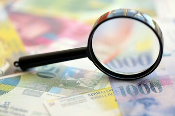 Swiss franc banknotes and magnifying glass. The current francs money bills with loupe lies on table