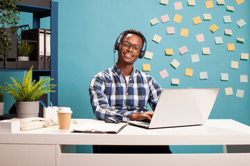 Smiling african american agent wearing a headset, happily assisting a client during a call in...