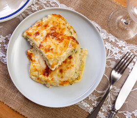 .Lasagna with minced fish and broccoli with lots of cheese. Casserole with golden crust, served with slices of bread and utensils. .
