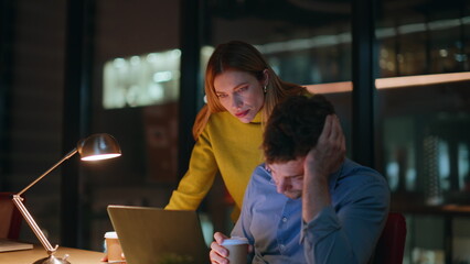 Worried coworkers looking laptop at dark office closeup. Woman helping man