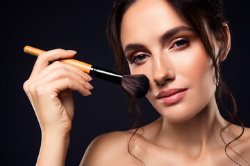 Obraz premium Young woman applying makeup with a brush on her flawless skin, enhancing natural beauty