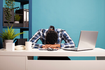Overworked male entrepreneur collapsed on his office desk from fatigue after long work hours,...