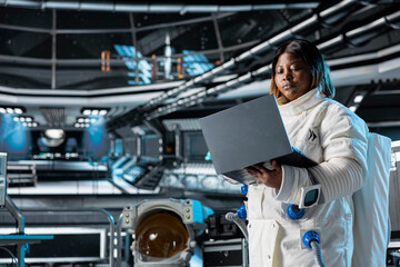 Astronaut using laptop to confirm suit integrity, monitoring life support systems. Orbital station...