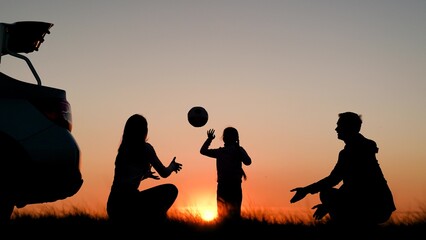 Family traveling by car with child. Cheerful family playing with ball in nature near car. Parents, child stopped for rest by car. Father, mother, child traveling by car, playing in front of sunset sky