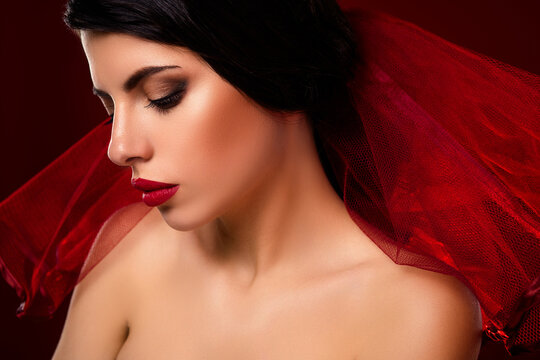 Passionate portrait of a beautiful woman with vibrant red veil and glamorous makeup on a dark background