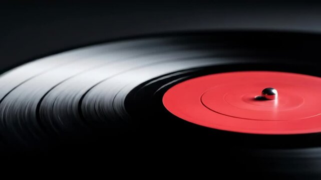 A seamlessly looping close-up video of a black vinyl record with a red label spinning on a dark background, showing light reflecting on the grooves.