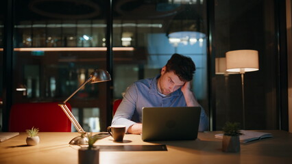 Overworked manager browsing laptop at night workspace. Tired businessman burnout