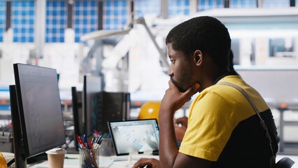 Black worker programming robotic assembly line in solar cell factory, working with high tech...