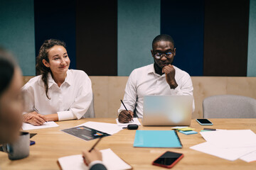Young businesswoman and Black businessman focused on analytics and insights during modern team meeting, blending digital tools with creative collaboration for tech-driven decisions