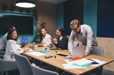 Diverse business team discussing project strategy, young man leaning over laptop while colleagues...