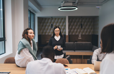 Young professionals collaborate in a shared workspace, using smartphones and laptops while...