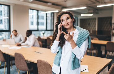 Cheerful young Caucasian woman in white shirt speaking on phone, using gestures during business...