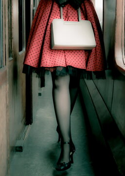 A woman in a red polka dot skirt and black heels walks down a train aisle.