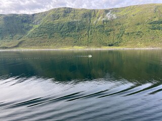 Calm sea with lone boat and steep green hilly coastline behind. 