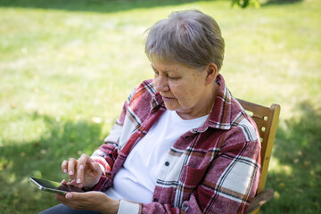 Senior woman using smartphone with concentration while sitting outside in park, concept of digital literacy, theme of aging, technology, independence