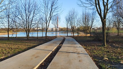 There is a concrete slabs path to the lake shore along the willows. A ripple on the water. On the...