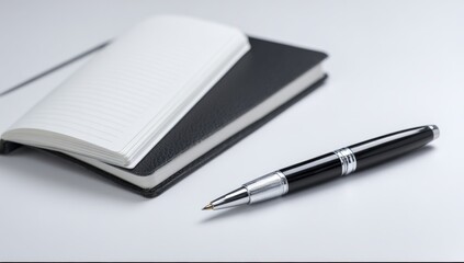Close-up of open notebook with lined pages and black cover alongside a black and silver retractable ballpoint pen on smooth white surface for planning and note-taking background