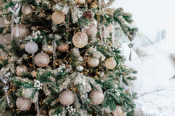 Christmas tree adorned with silver and gold ornaments in a cozy bedroom setting
