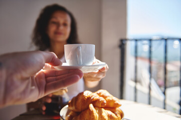 Warm summer morning featuring freshly brewed coffee, buttery croissants, and serene joy shared with a companion on a sunny balcony with a pleasant, scenic background.