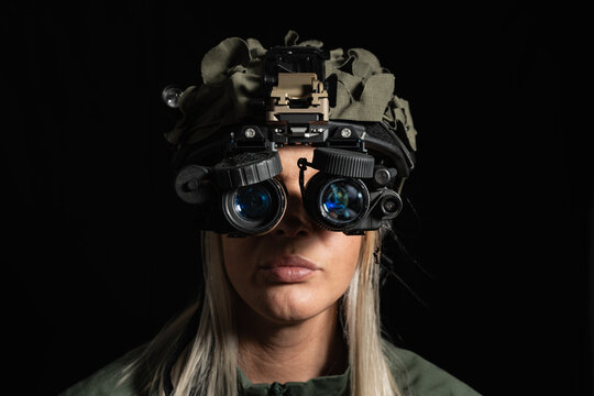 A female soldier in a modern tactical helmet and night vision goggles looks at the camera on a black background. Special forces concept.