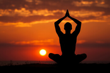 Silhouette of a person doing yoga in lotus pose against a dramatic sunset. A serene and spiritual shot of inner peace and balance. Meditation, mindfulness, healthy lifestyle.