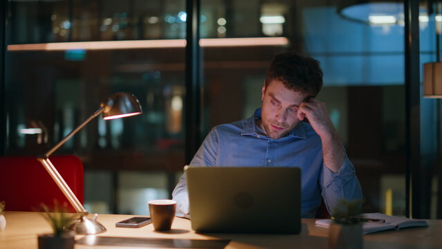 Remote worker browsing laptop at night workplace feeling burnout closeup.