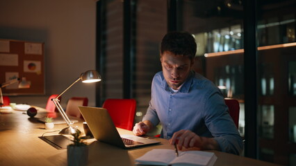 Pensive startuper working project overtime sitting night office room closeup.