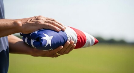 Hands holding a carefully folded United States flag against a bright outdoor setting with blurred