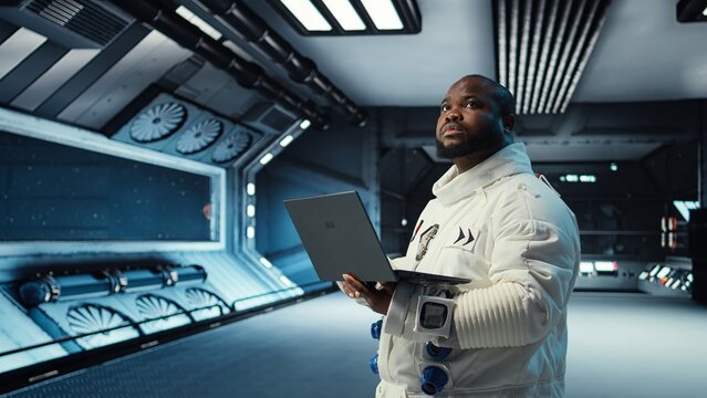 Astronaut in spacecraft using laptop to run telemetry data analysis. Man in spaceship wearing spacesuit analyzing mission logs on notebook during planetary exploration, camera A