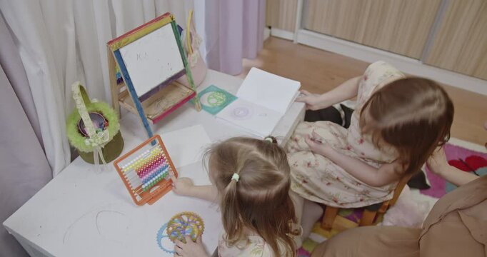A mother and her two daughters enjoy quality family time together at home, drawing and playing with an abacus and spirograph.