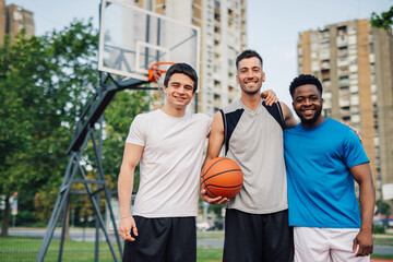 Three male basketball players posing together after game on outdoor court