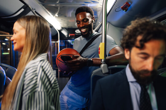 Young basketball player using smartphone on bus with passengers