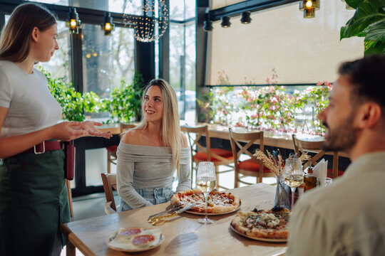 Waitress suggesting pizza to couple in restaurant - Powered by Adobe