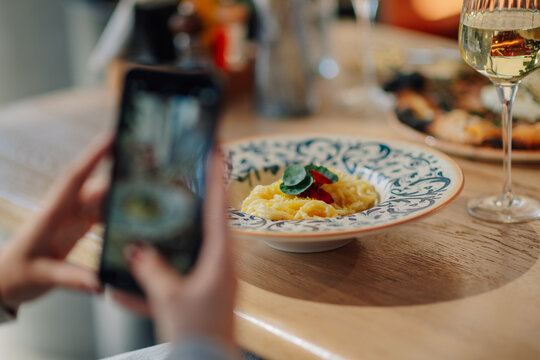 Woman taking photo of gourmet pasta dish with smartphone in restaurant