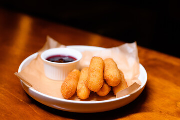 Crispy cheese sticks served on parchment paper in a white plate with a side of berry sauce. Perfect snack or appetizer, great for sharing and dipping