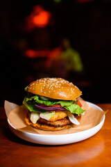 Juicy hamburger with lettuce, tomato, onion, cheese, and a sesame seed bun served on parchment paper in a white plate. Classic American fast food with a gourmet twist