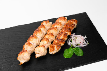 Two skewers of juicy grilled pork shashlik with a golden crust, served on a black slate plate accompanied by fresh spinach leaves and pickled onion garnish