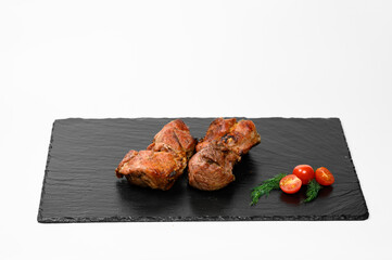 Two juicy roasted pork chunks with a golden-brown crust are placed on a black slate tray. Fresh...