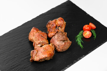 Two juicy roasted pork chunks with a golden-brown crust are placed on a black slate tray. Fresh...