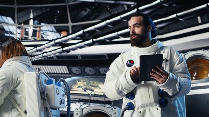 Astronaut reading mission plan on tablet before stepping out for scheduled operations outside space...
