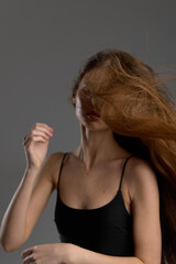Obraz premium woman with long hair in black tank top moves hair dynamically against gray background, capturing motion and natural beauty in soft lighting.