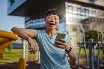 Japanese woman in a sportswear stand in park and use mobile phone