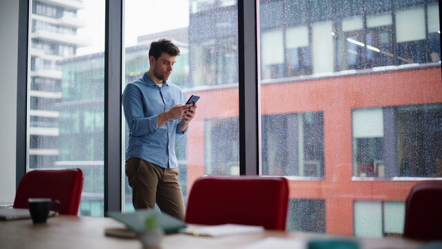 Focused startuper texting cellphone in office conference room. Serious man