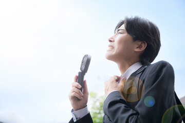 暑い中汗をかく営業する大変なビジネスマン　ハンディファンで涼むイメージ　夏の外回りは熱中症に注意
