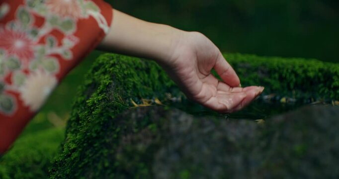 A Japanese woman in a kimono draws water from a stone. Close-up of her hand, unrecognizable person