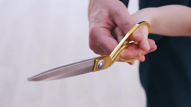 Close-up of golden scissors as an adult and a child cut a red ribbon together, symbolizing a meaningful moment, intergenerational unity, and the ceremonial nature of the event

