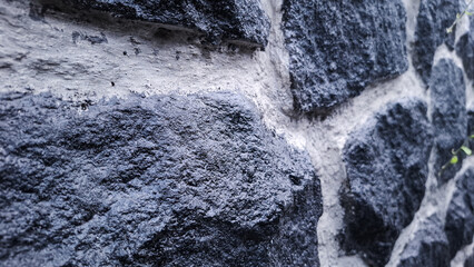 Fototapeta premium A close-up view of a stone wall, featuring dark, irregular-shaped rocks mortared together with light-colored grout, highlighting the rough texture and natural variations