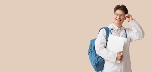 Male medical student with backpack and laptop on beige background with space for text